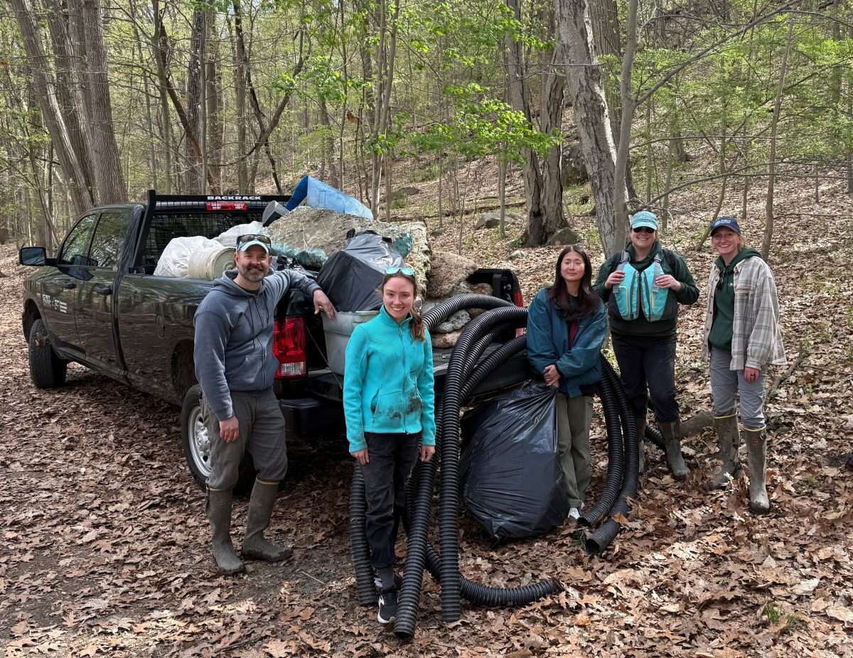 Five people stand in front of a pickup truck   with a truck bed full of trash and debris.